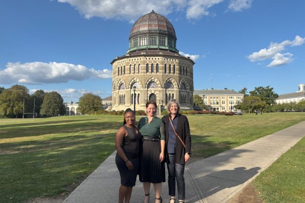 Three presenters standing in front of a building on campus